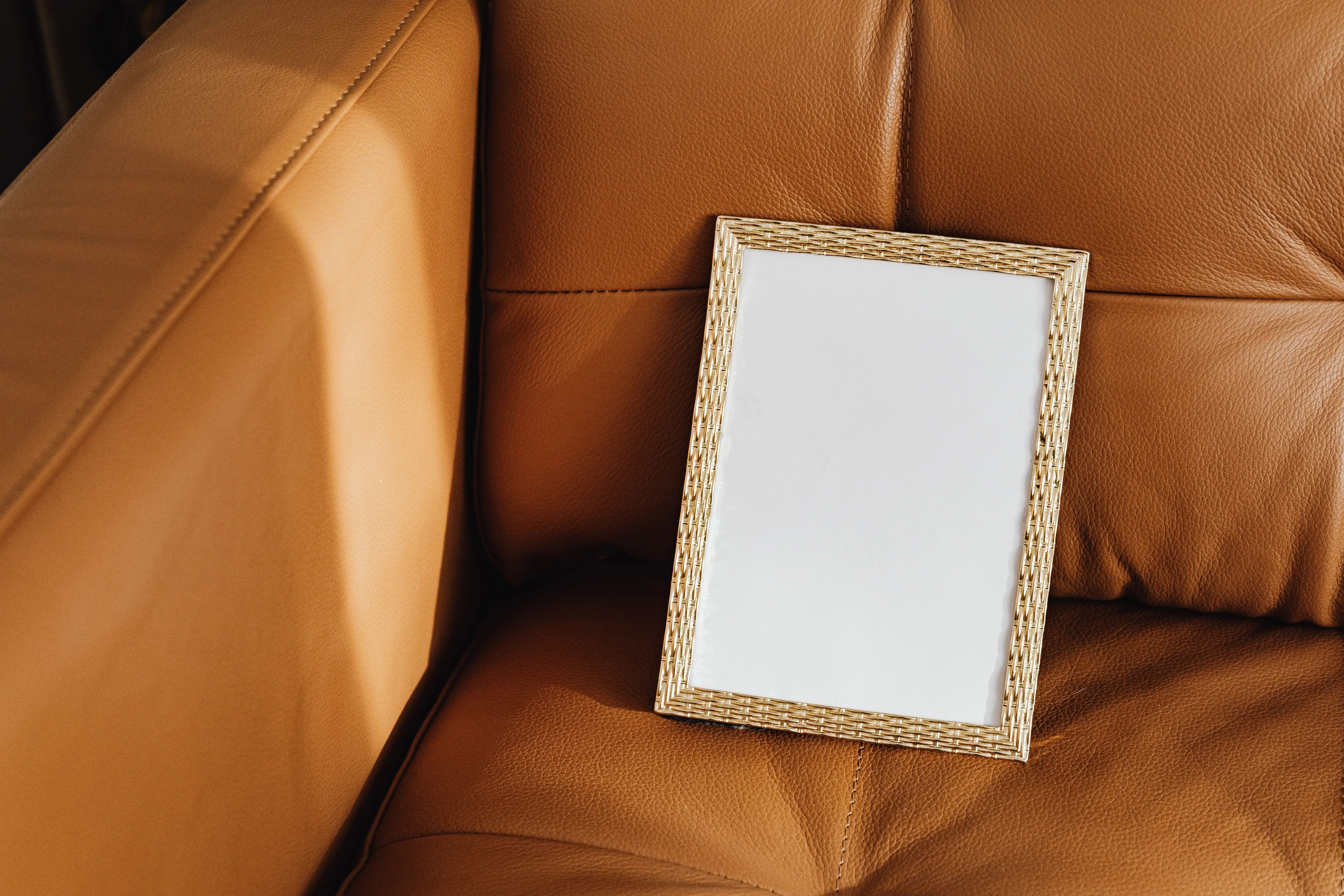 brown sectional sofa A blank picture frame rests on a brown leather sofa, perfect for mockups.