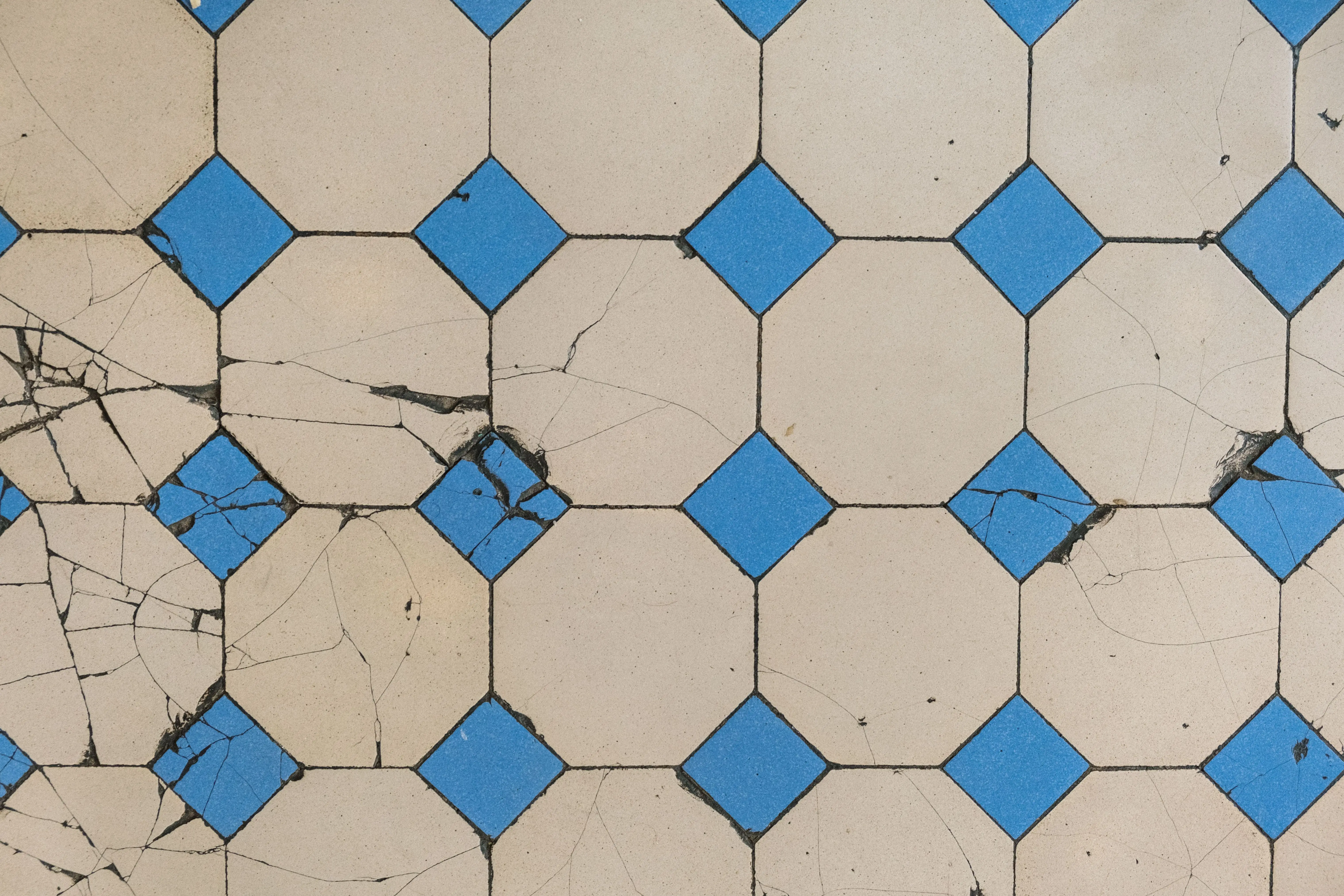 blue floor tile Top view of a cracked geometric tile pattern featuring blue diamond tiles on a beige background.