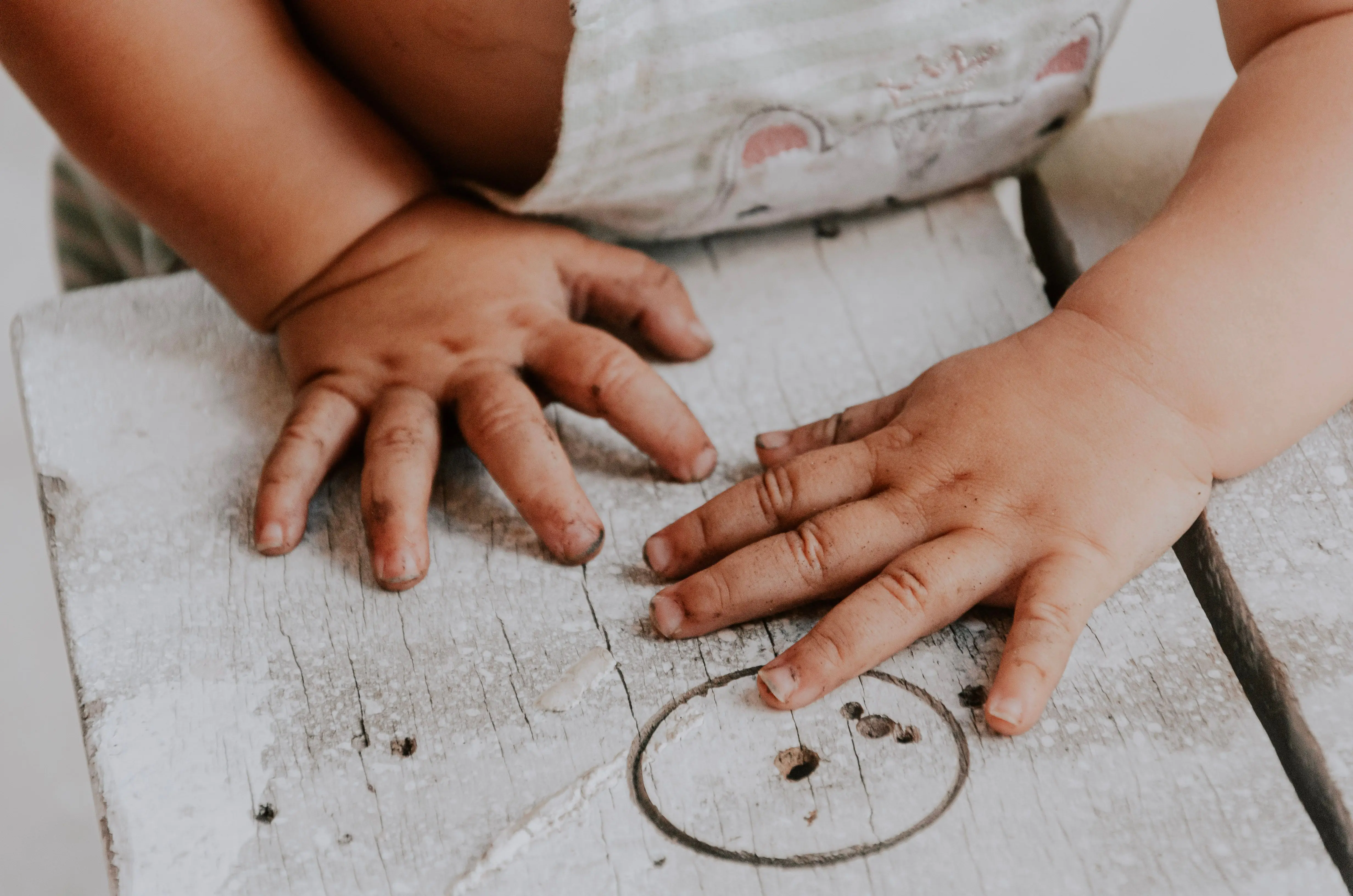 christmas handprint crafts Adorable toddler exploring with dirty hands on a rustic wooden surface.