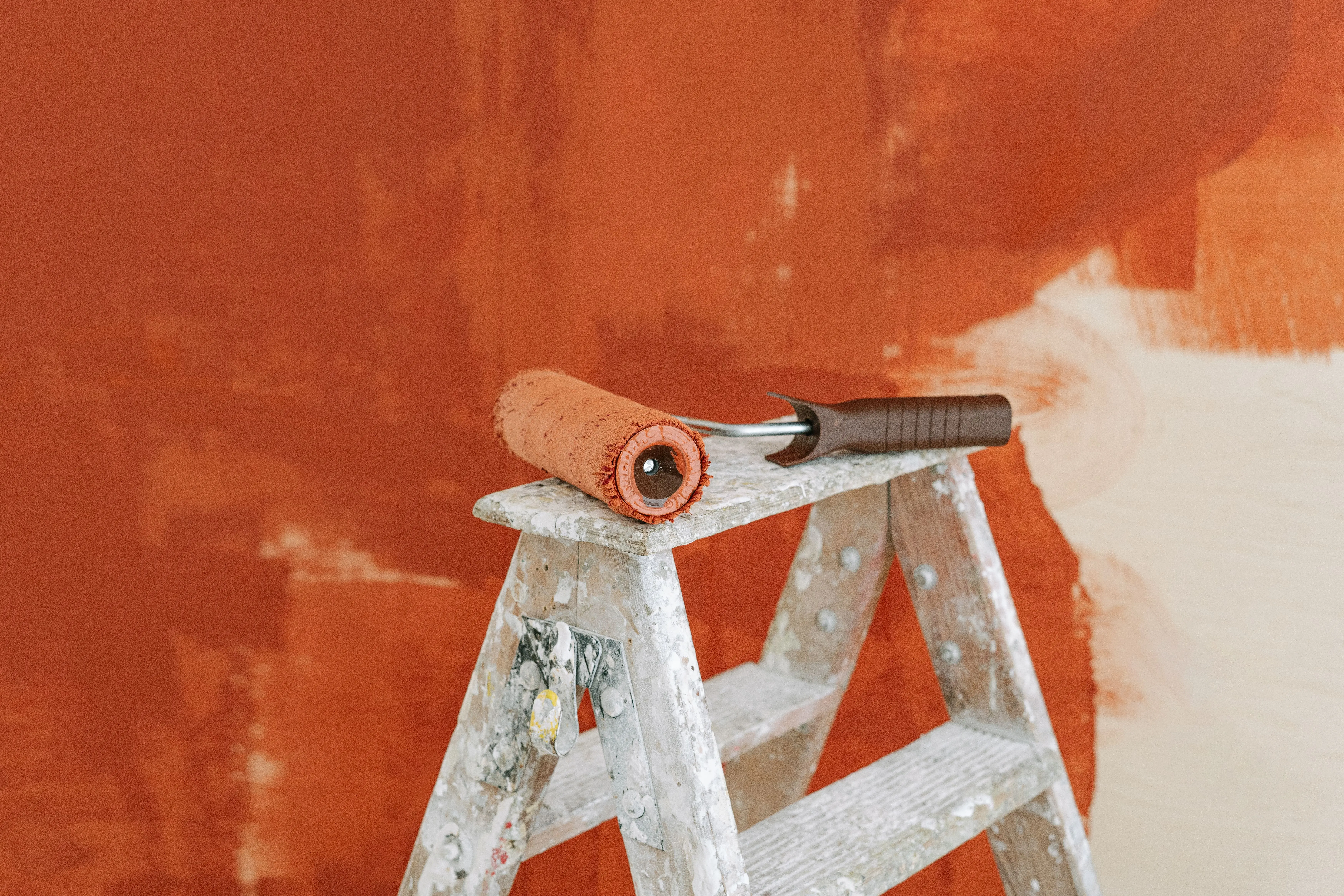cinnamon slate color Paint roller on a ladder with a partially painted red wall in the background.