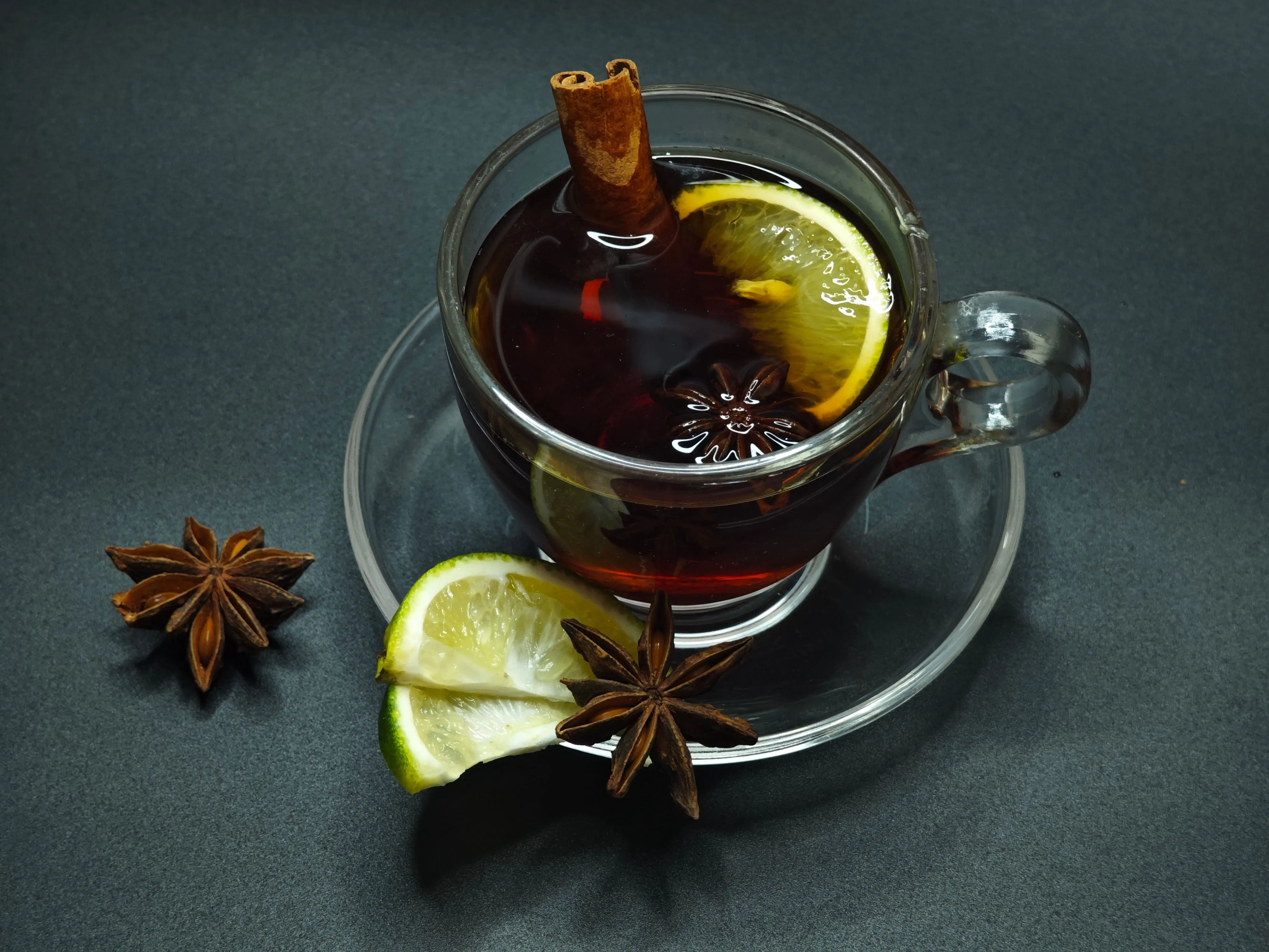 cinnamon slate Glass of spiced tea with lemon slice, cinnamon stick, and star anise on a dark background.