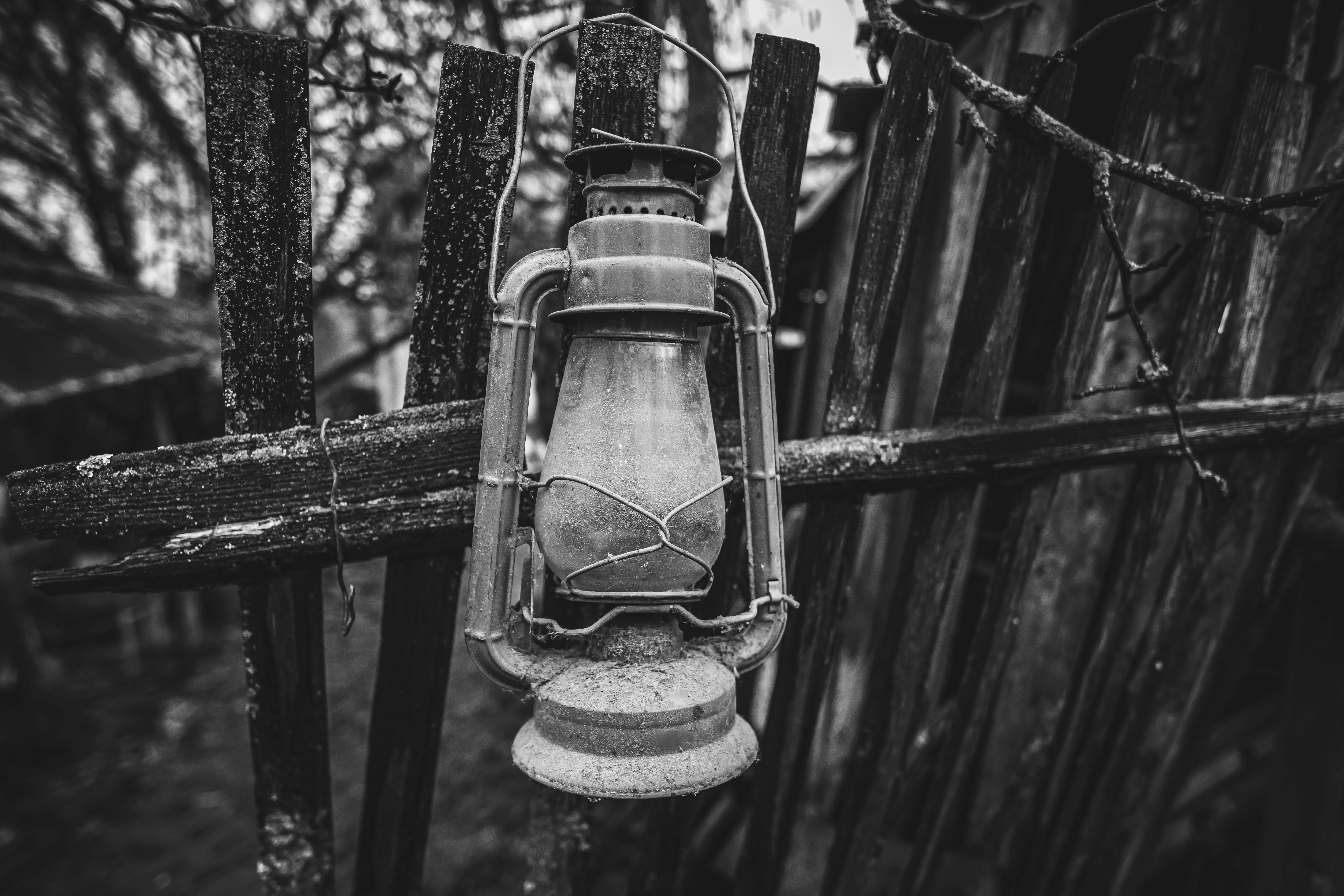 farmhouse light fixture Monochromatic image of an old kerosene lantern hanging on a weathered wooden fence in rural Slovakia.