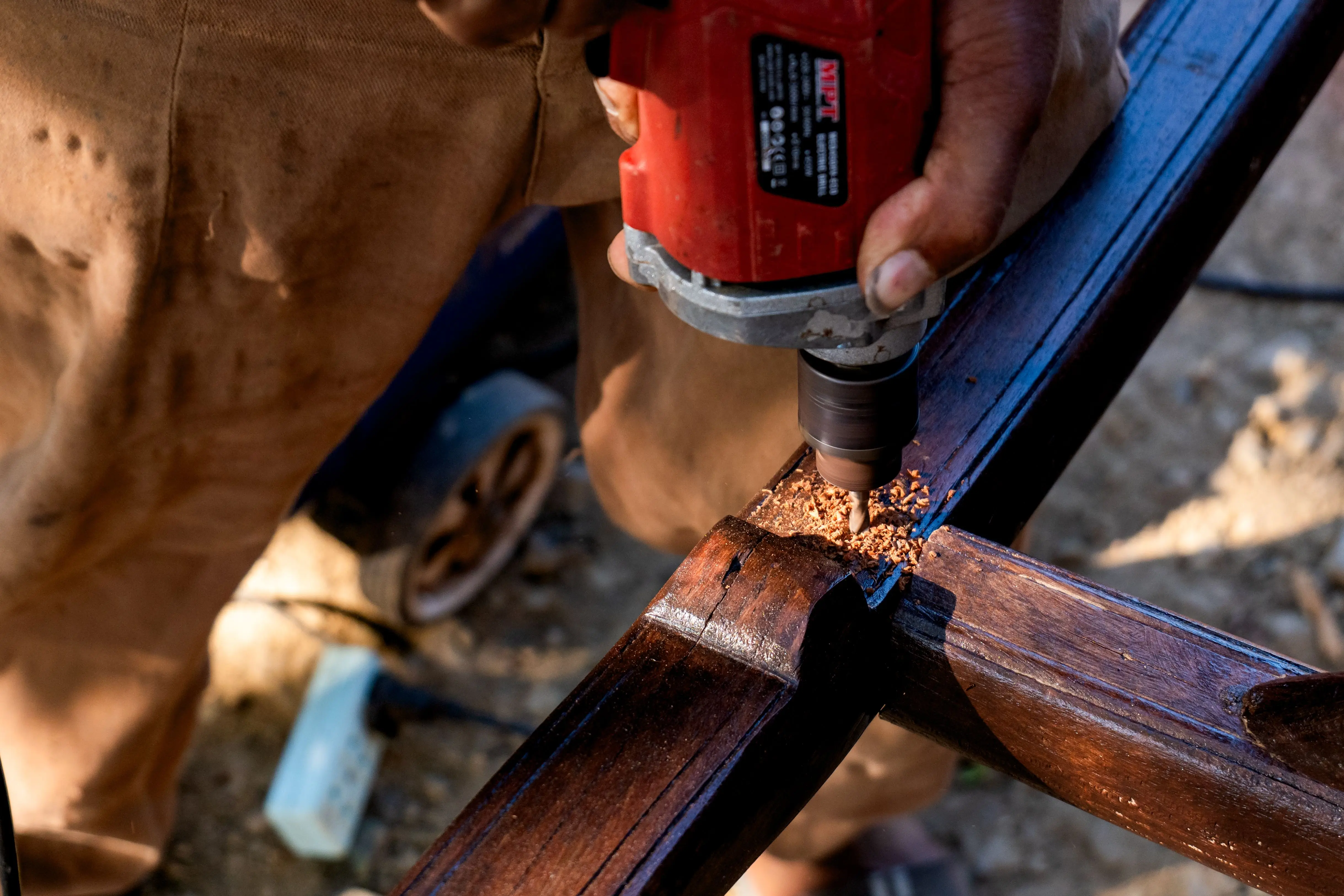 extension dining table Close-up of a person using a drill on a wooden beam during a carpentry project outdoors.