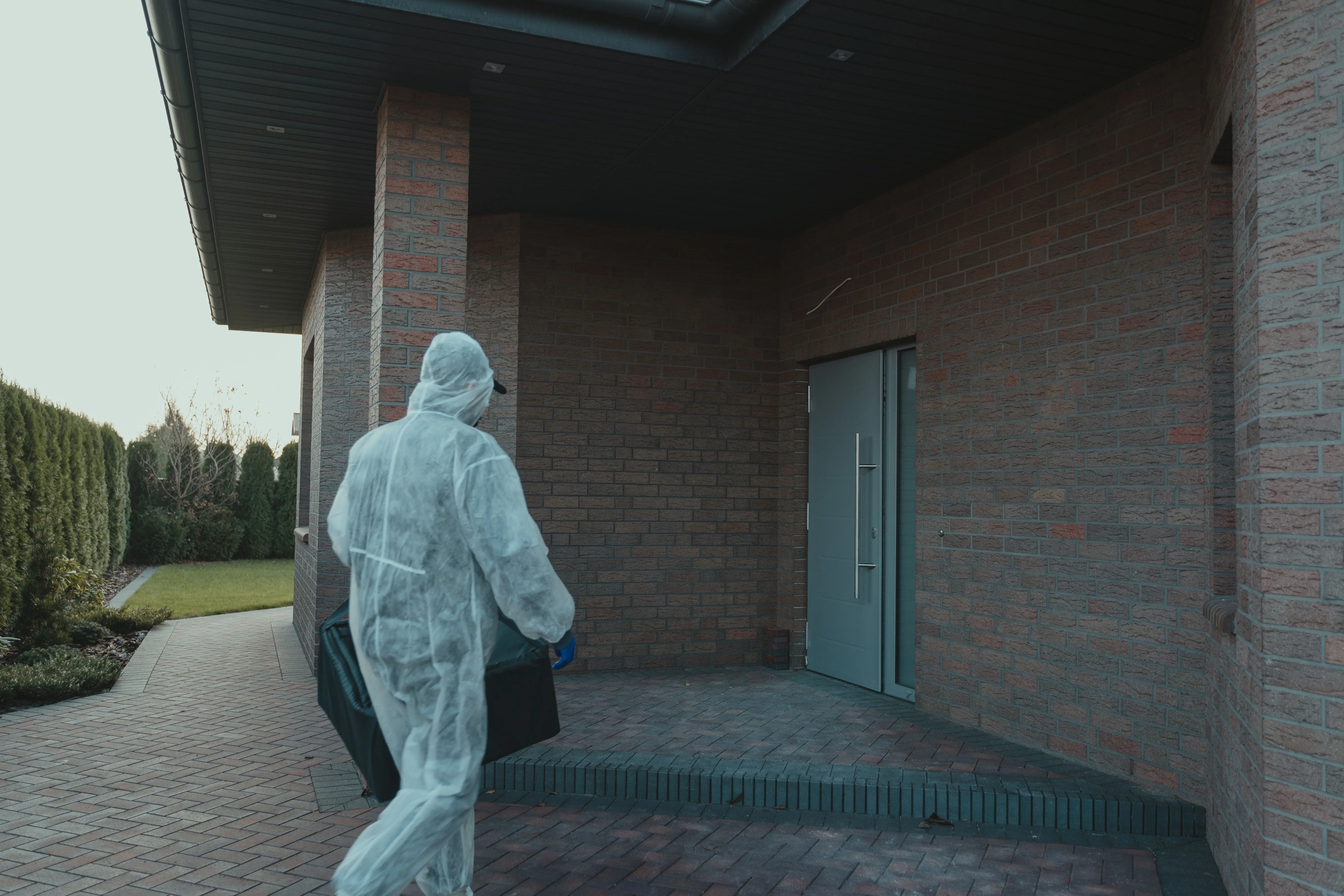 cost of exterminator A person in PPE gear delivering a package to a contemporary brick house.