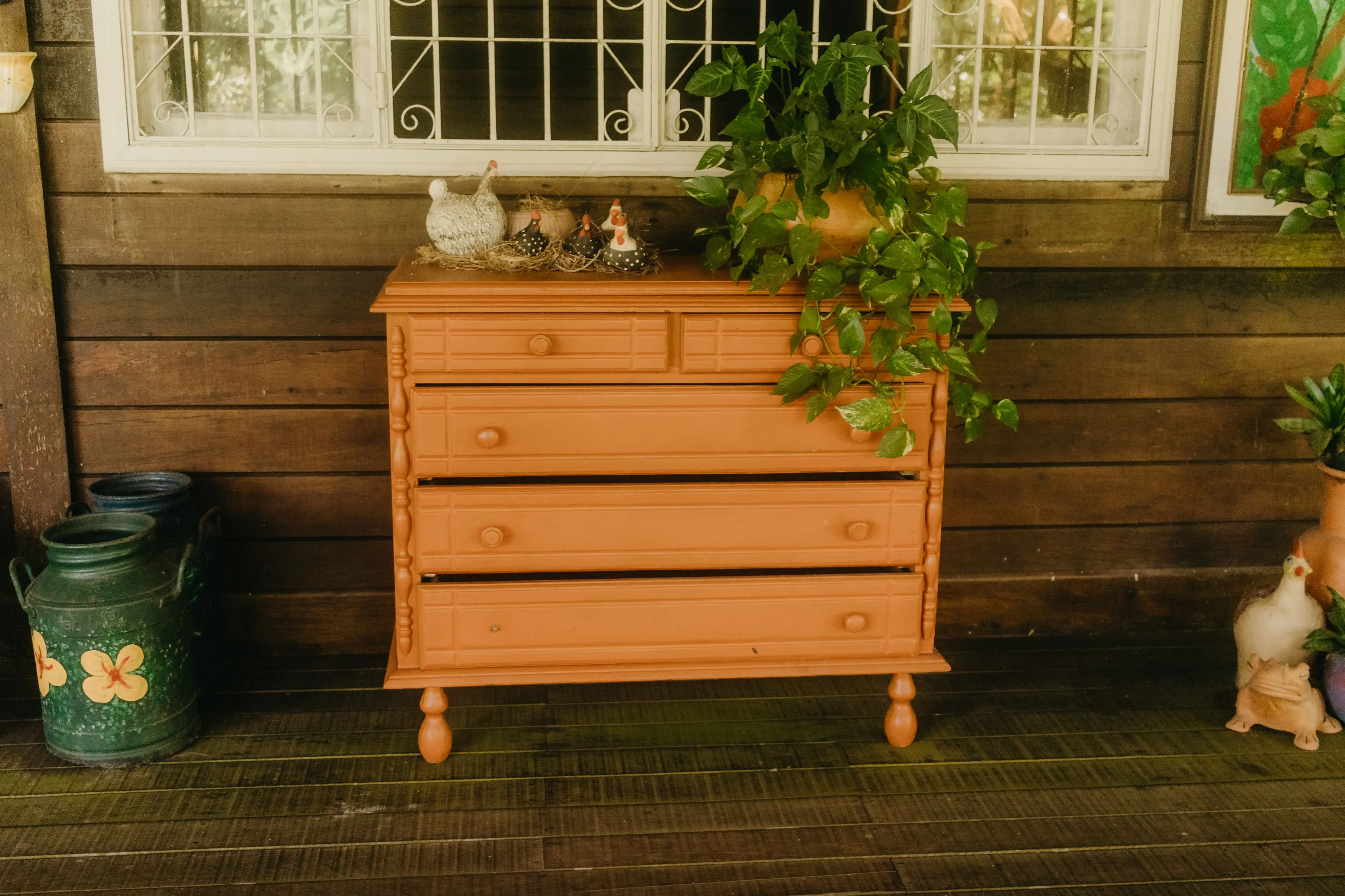 farmhouse wall art Wooden dresser painted orange with plants and ceramic hens, perfect for rustic decor.