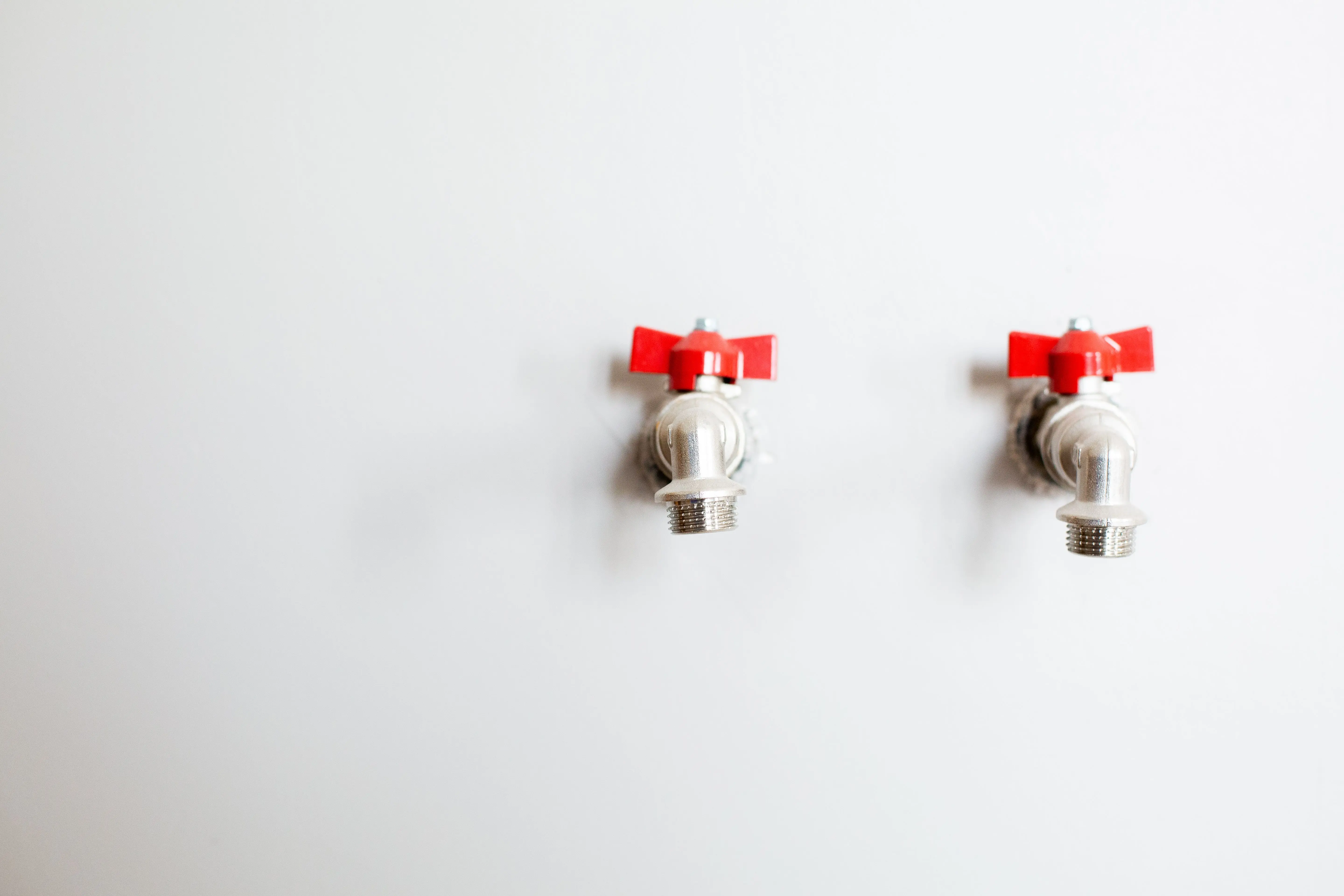 bathroom sink parts Close-up of two metal faucets with red handles against a white wall, showcasing plumbing detail.