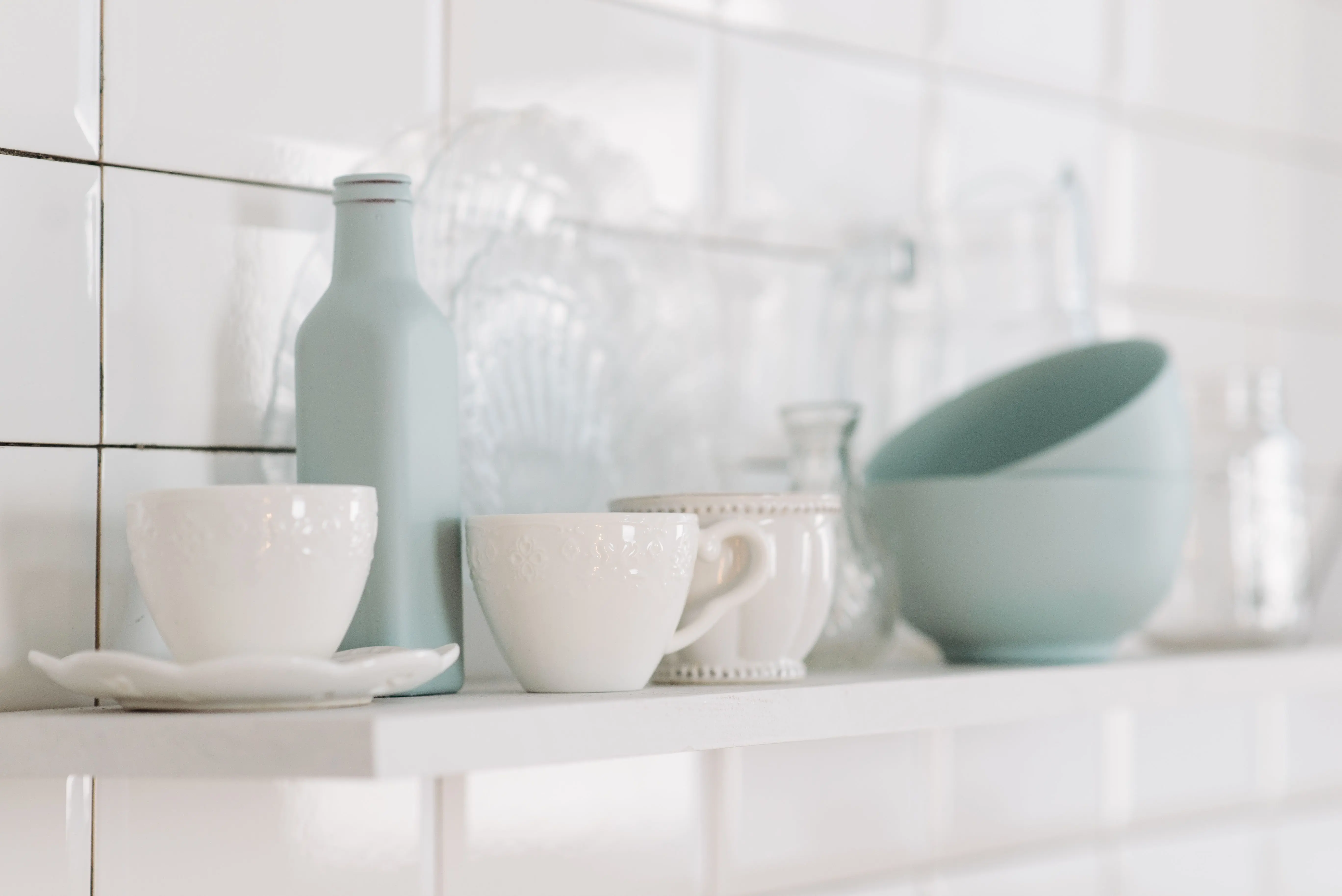 blue subway tile Elegant display of white and pastel kitchen pottery on a shelf in a minimalist style.