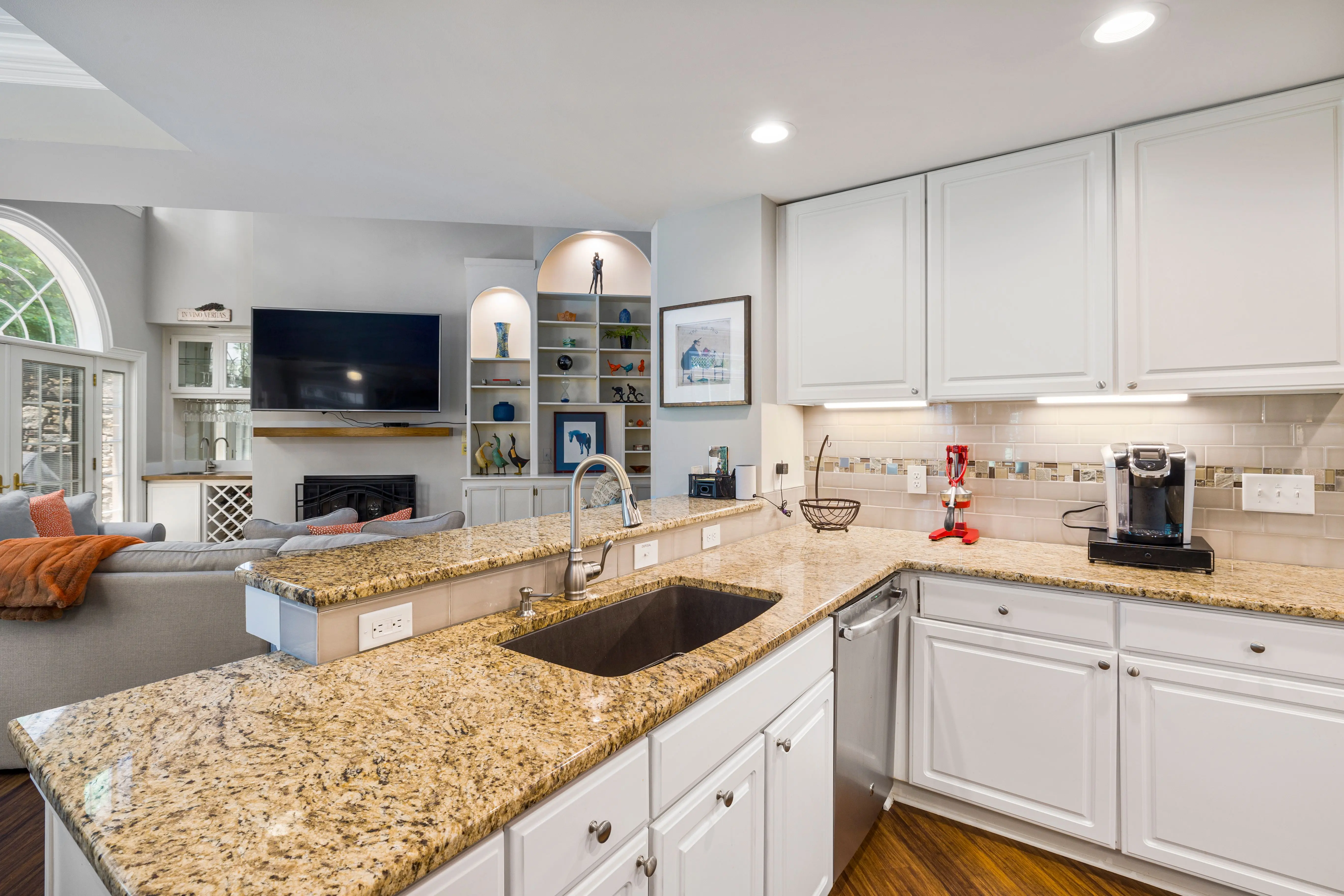 gray granite countertops A modern kitchen with granite countertops opens into a stylish living room, featuring elegant furniture and built-in shelves.