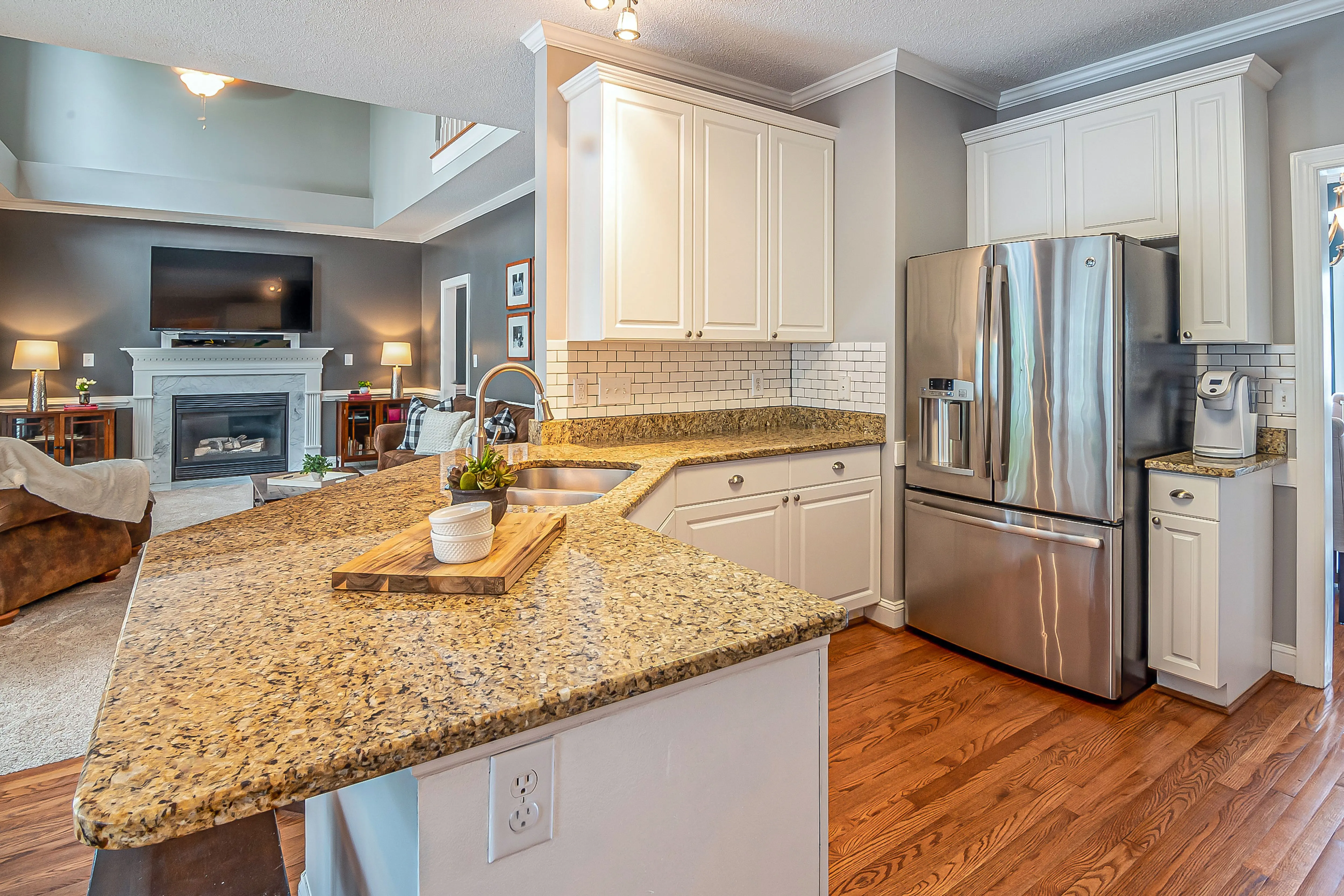 gray granite countertops Luxurious open-concept kitchen with granite countertops and modern appliances, flowing into a cozy living room with a fireplace.