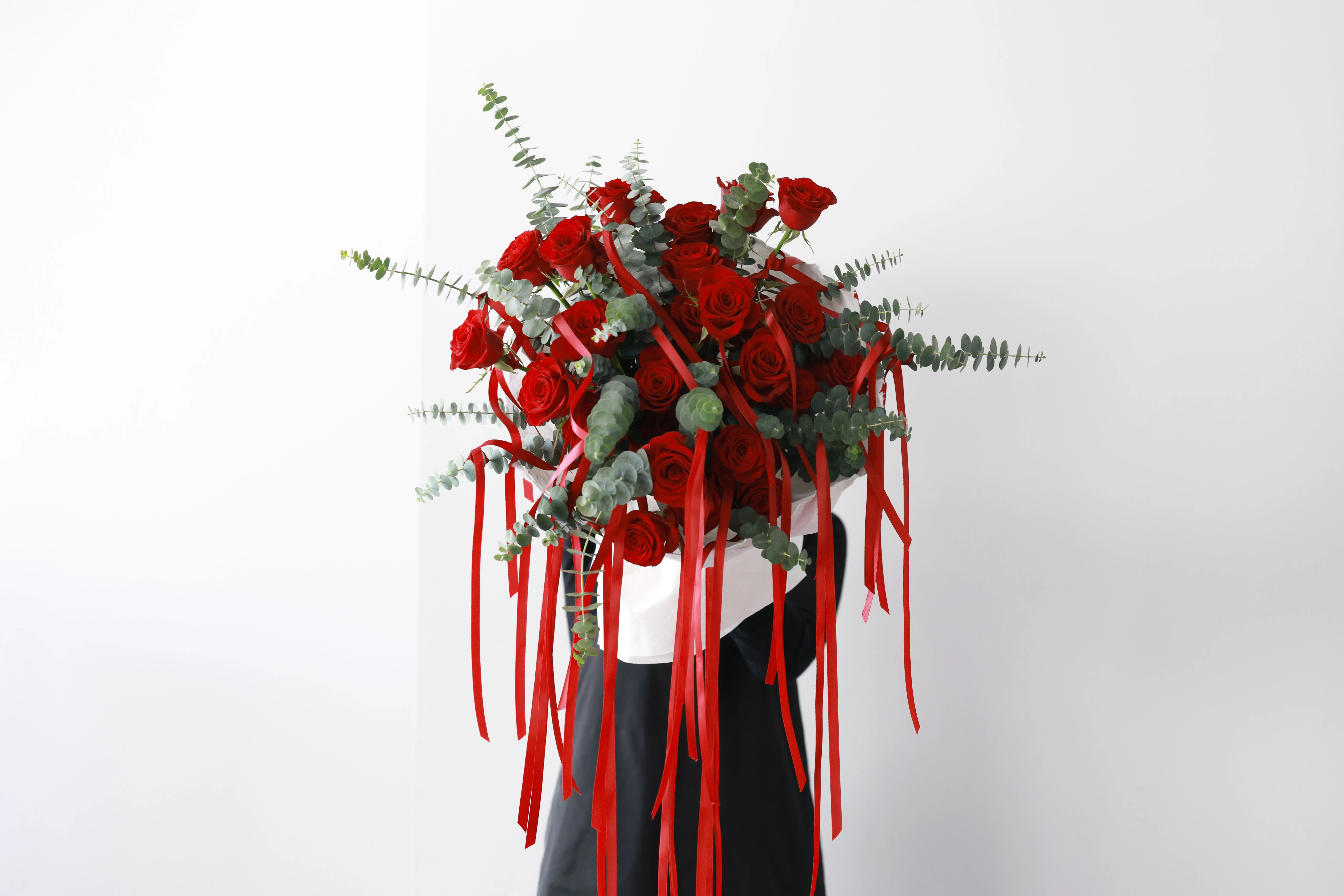 big bouquet of roses A stunning bouquet of red roses and eucalyptus, adorned with red ribbons, held by a person in formal attire.