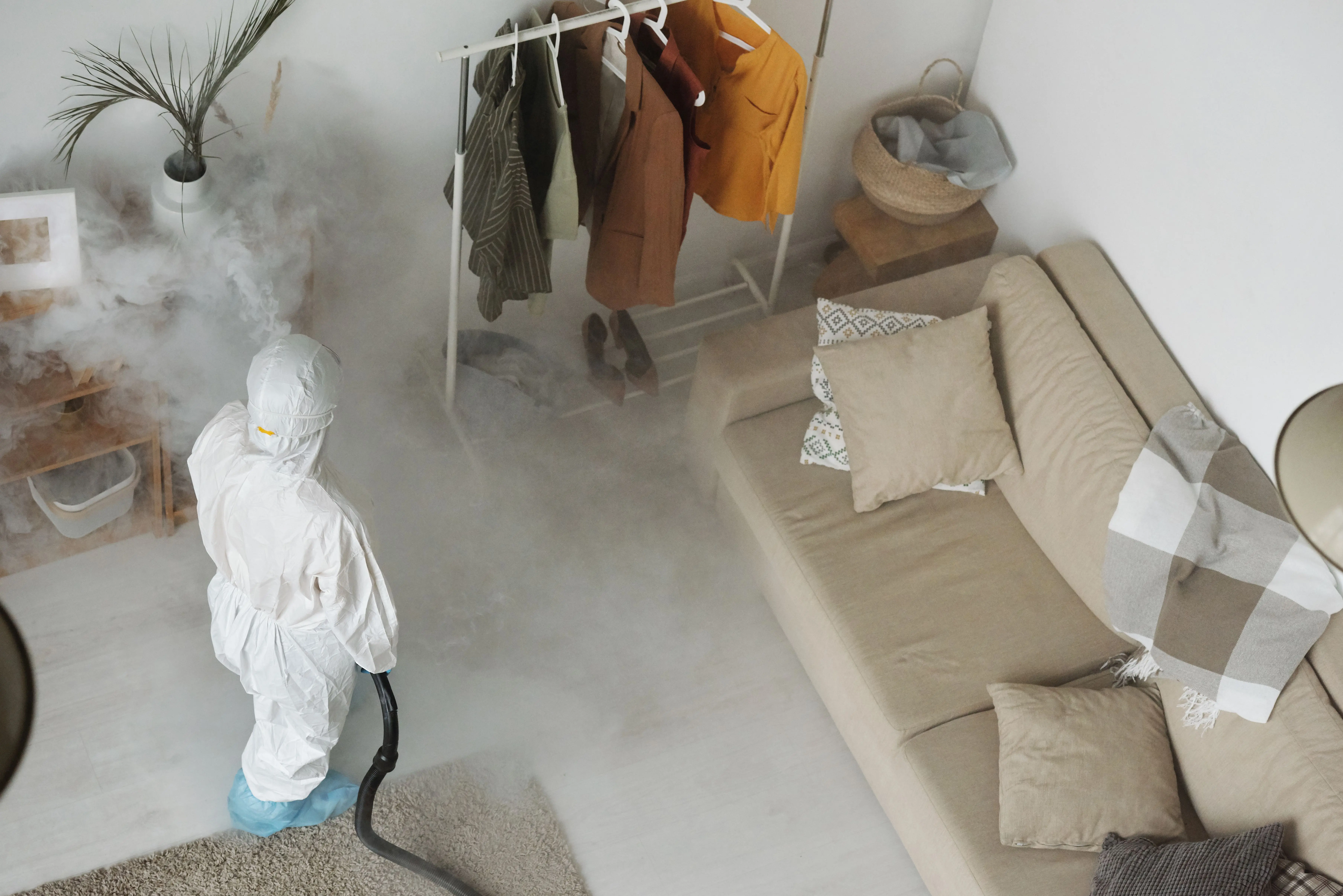 cost of exterminator Professional in protective gear sanitizing a modern living room with a fumigation machine.