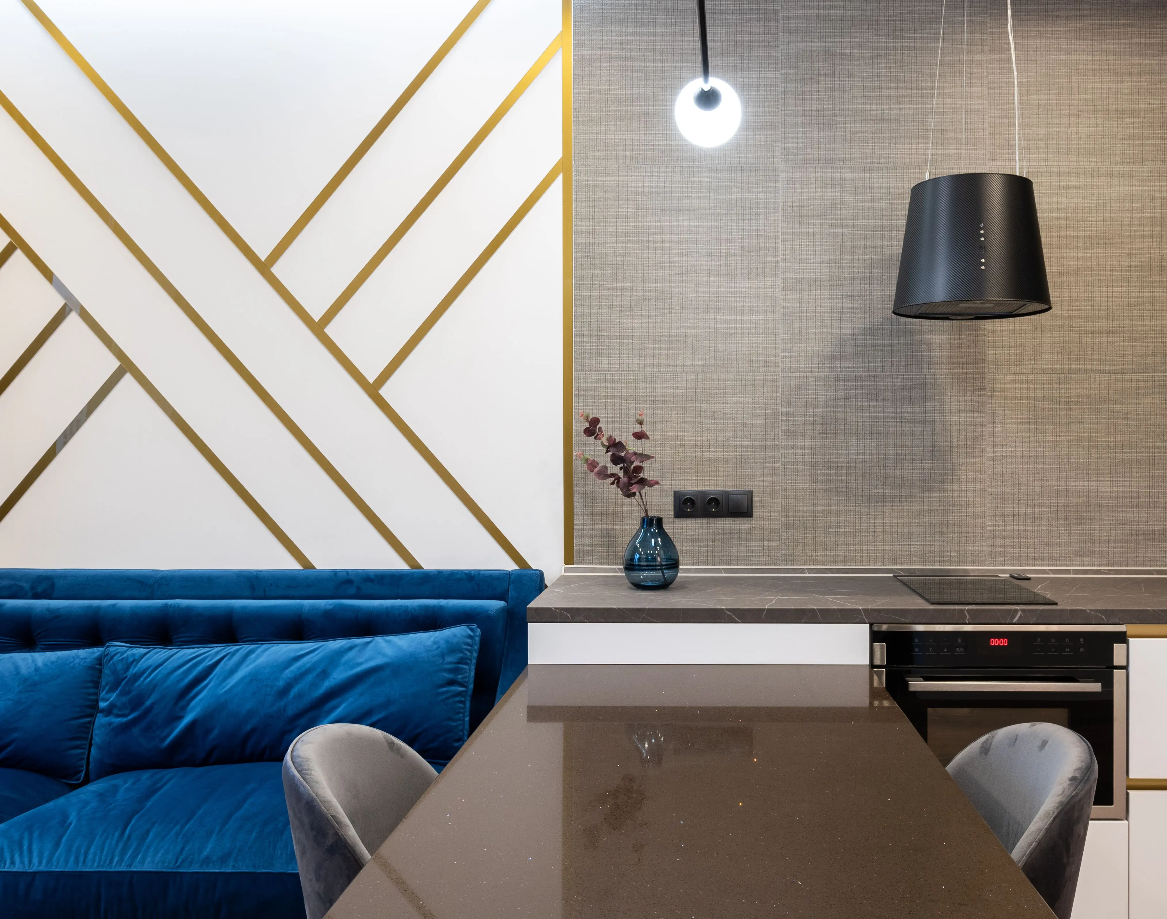 blue backsplash Interior of bright modern flat with table and chairs near blue couch and kitchen with cabinet and counter with oven and stove near vase with flowers and lamp