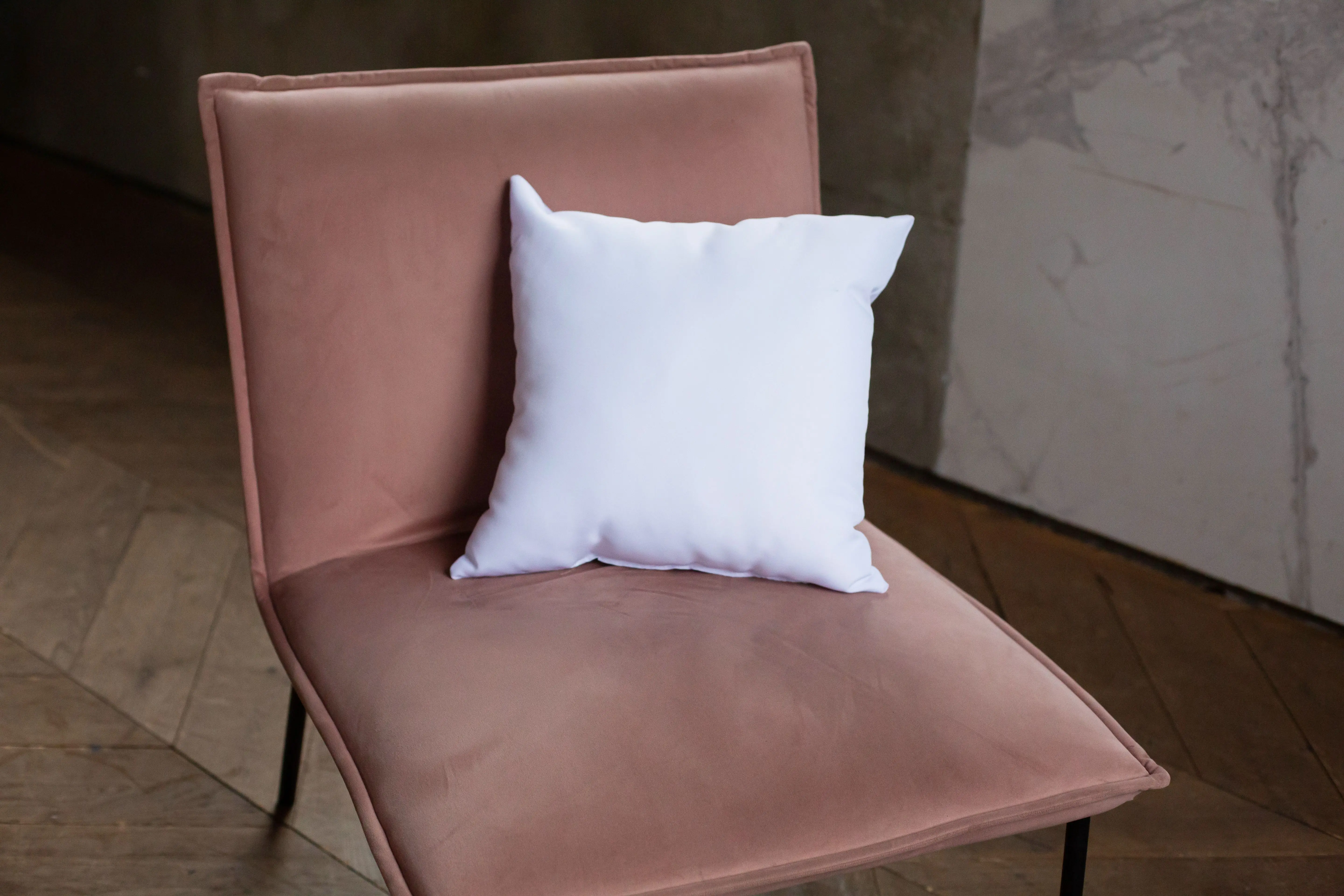 blue throw pillow A stylish beige chair with a white pillow, set against a textured wall in a rustic indoor environment.