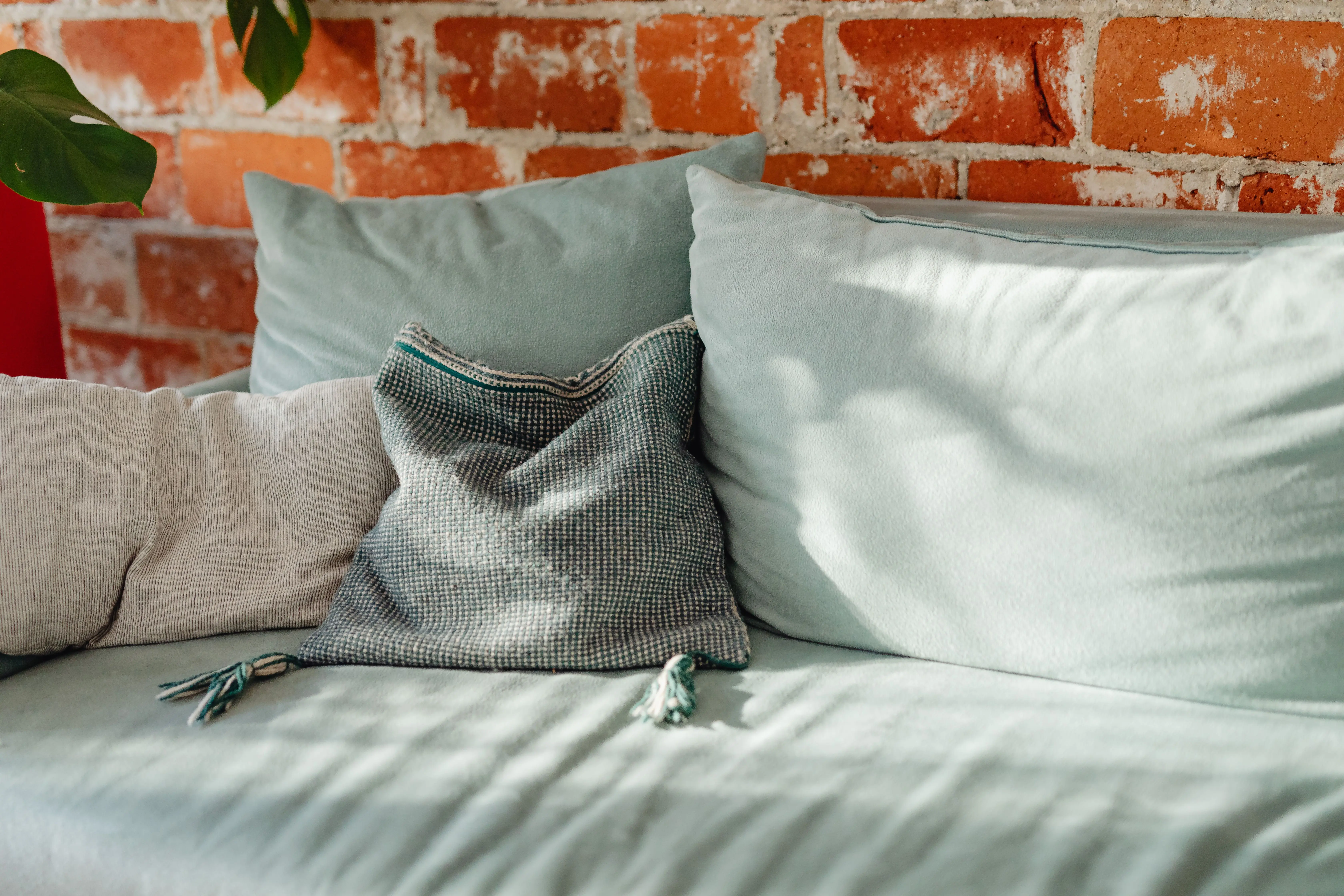 blue throw pillow A stylish teal sofa with cushions against a rustic brick wall, perfect for cozy interiors.